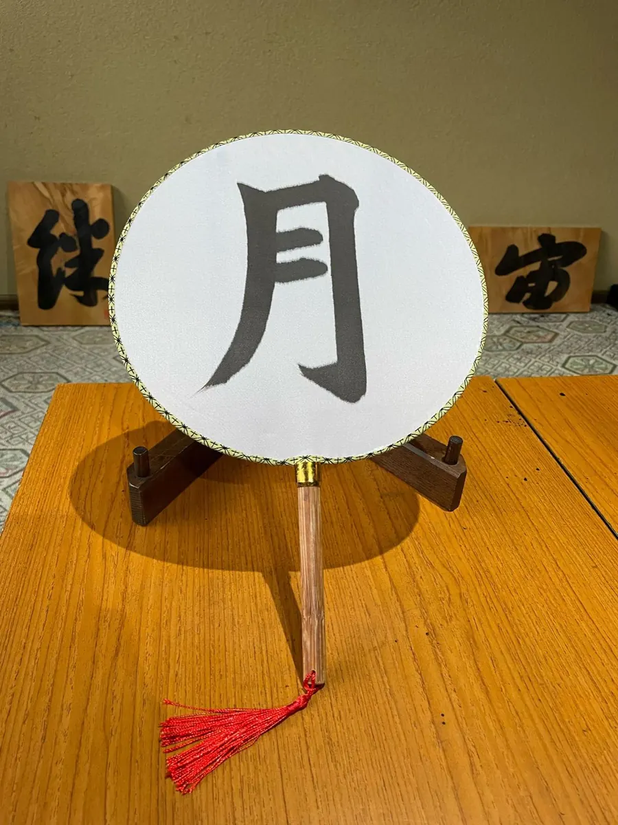An uchiwa fan with the kanji 月 (moon) written in sumi ink